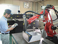YAGレーザ溶接ロボットYLR-15002のティーチング作業をする入社4年目の古関智広さん。月間70時間から120時間稼働する。