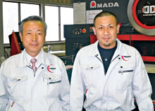 EM-2510NT の前で鈴木信夫社長(左)と子息の鈴木貞晴工場長(右)