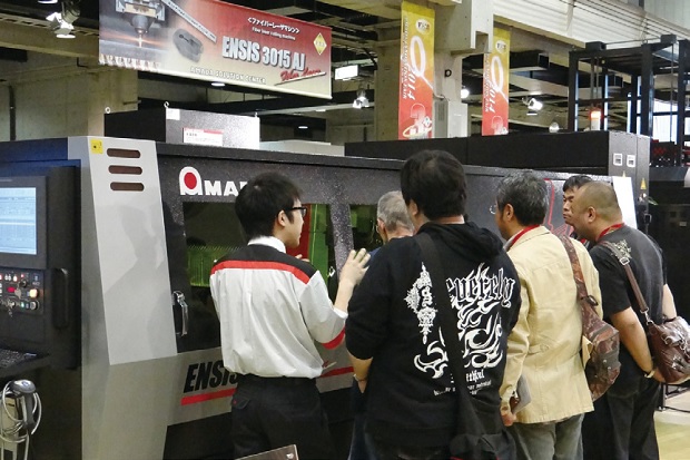 画像：変種変量・省エネ・ワイドレンジ・ファイバーレーザマシンENSIS-3015AJの実演加工を熱心に見る来場者
